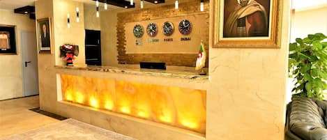 Una zona de recepción con mostrador de mármol, relojes de pared, un retrato enmarco y una planta en maceta.