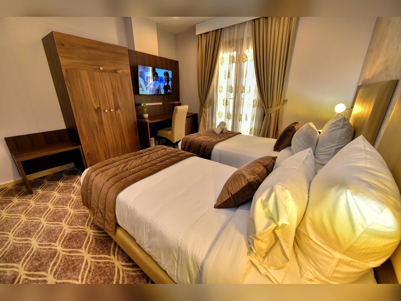 Habitación de hotel con dos camas, televisor, escritorio y armario.