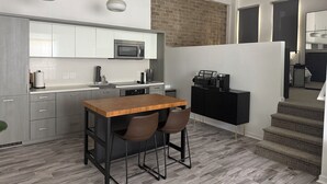 Uma cozinha moderna com uma mesa de madeira e banquetas, micro-ondas e parede de tijolos.