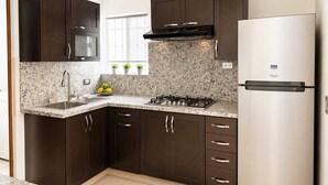 A kitchen with dark cabinets, a stainless steel refrigerator, a gas stove, and a granite countertop. - Entire House | Escobedo | North Monterrey (Ciudad General Escobedo)