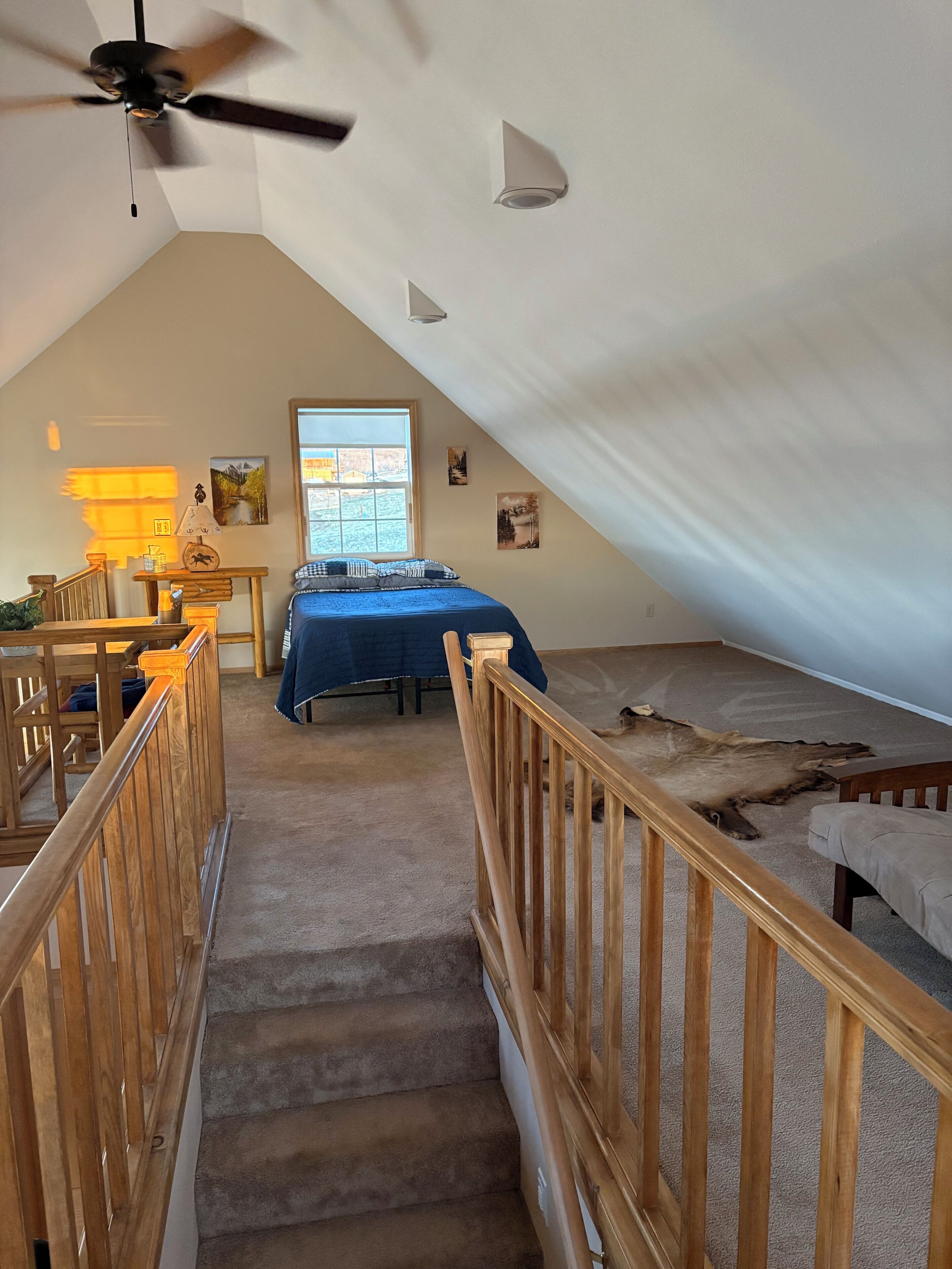 Une chambre à coucher avec un lit, un bureau, une chaise, une fenêtre et un escalier.