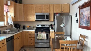 A kitchen with wooden cabinets, a stainless steel microwave, oven, and refrigerator, a dining table with chairs, and a patterned rug. - Pleasant 4-bedroom house in Centennial perfect for family getaways (Centennial)