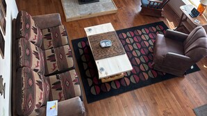 A loft-style living room with a wooden beam ceiling, a fireplace, a sofa, a chair, and a window with a view. - Pleasant 4-bedroom house in Centennial perfect for family getaways (Centennial)