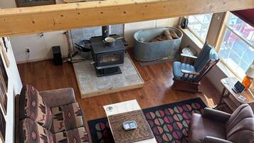 Un salon de style industriel, avec un plafond doté de poutres en bois, une cheminée, un canapé, un fauteuil et une fenêtre offrant une vue agréable.