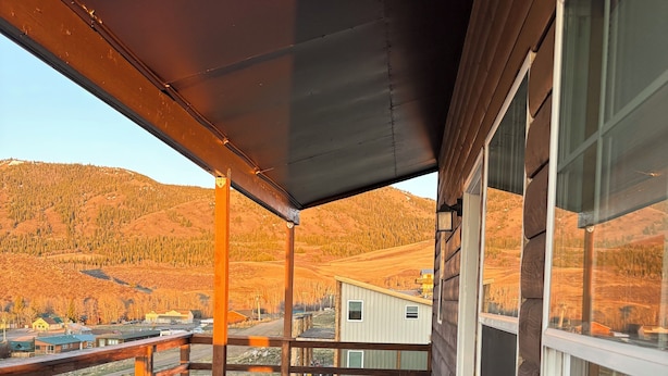 A wooden deck with a bench, a covered area, and a view of a hilly landscape. - Pleasant 4-bedroom house in Centennial perfect for family getaways (Centennial)