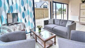 Una sala de estar con un sofá, sillones, una mesa de centro de vidrio y un televisor sobre un mueble.