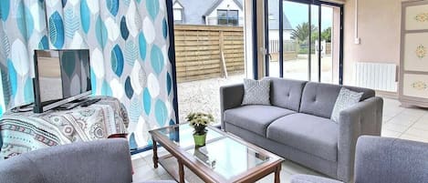 A living room with a sofa, armchairs, a glass coffee table, and a TV on a stand.