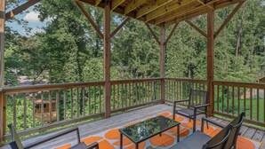 A covered outdoor area with a wooden deck, seating, and a view of a forest. - Design Lover’s 1br Suite (Atlanta)