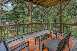 Ein überdachter Außenbereich mit Holzterrasse, Sitzgelegenheiten und Blick auf einen Wald.
