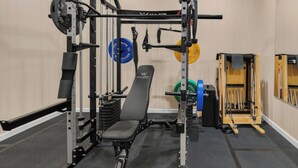 A gym with weightlifting equipment, a bench, and a squat rack. - Design Lover’s 1br Suite (Atlanta)