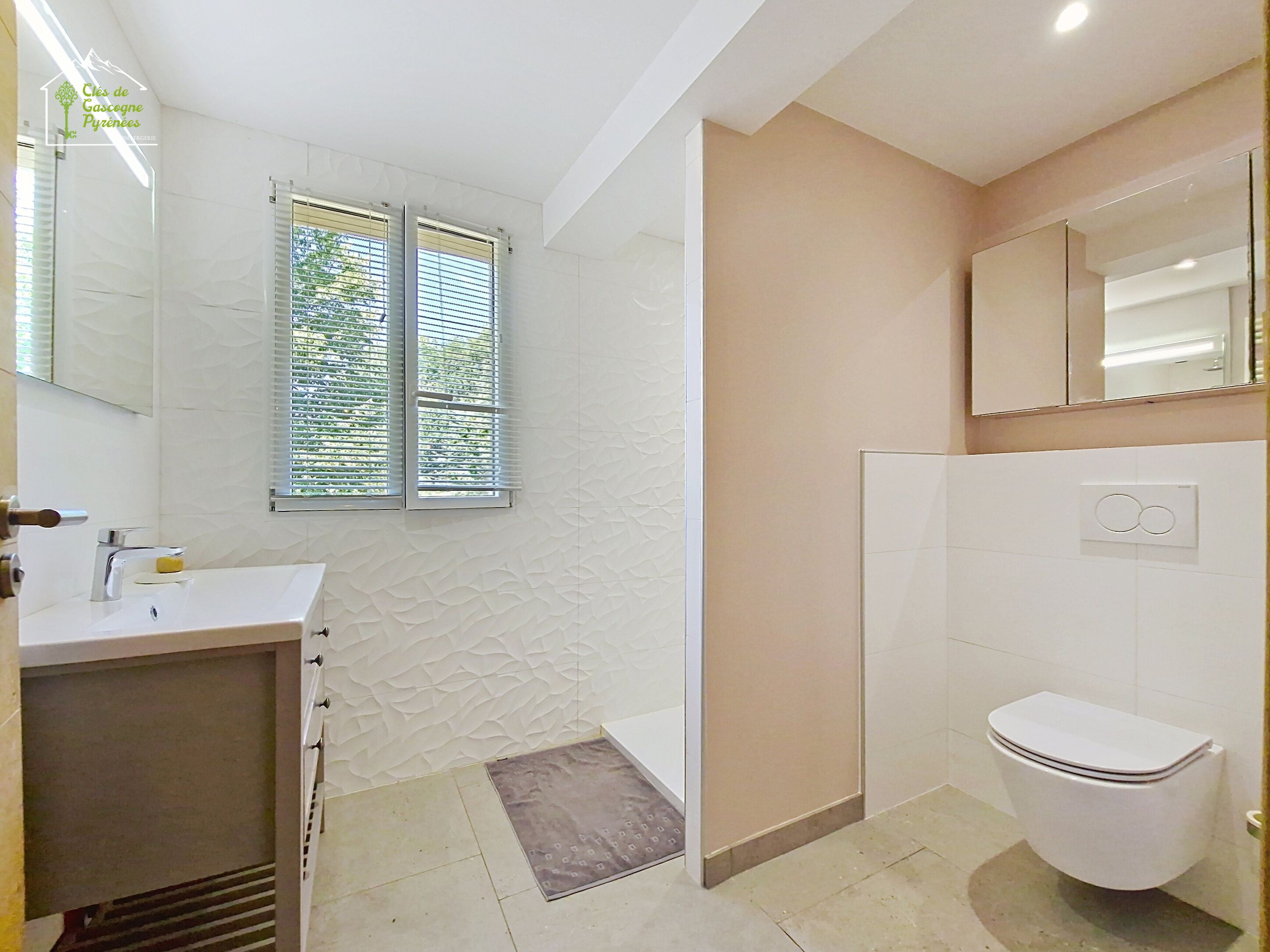 Une salle de bain avec un lavabo, des toilettes et une fenêtre équipée de stores.