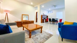 Ein geräumiges Wohnzimmer mit einer Couch, einem Couchtisch, einem Essbereich mit Stühlen, einem Bücherregal und einem Deckenventilator.