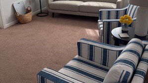Un salón con sofá, sillones a rayas, una lámpara de pie y una ventana con cortinas.