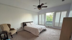 Ein Schlafzimmer mit Bett, Stuhl, Deckenventilator und großen Fenstern.
