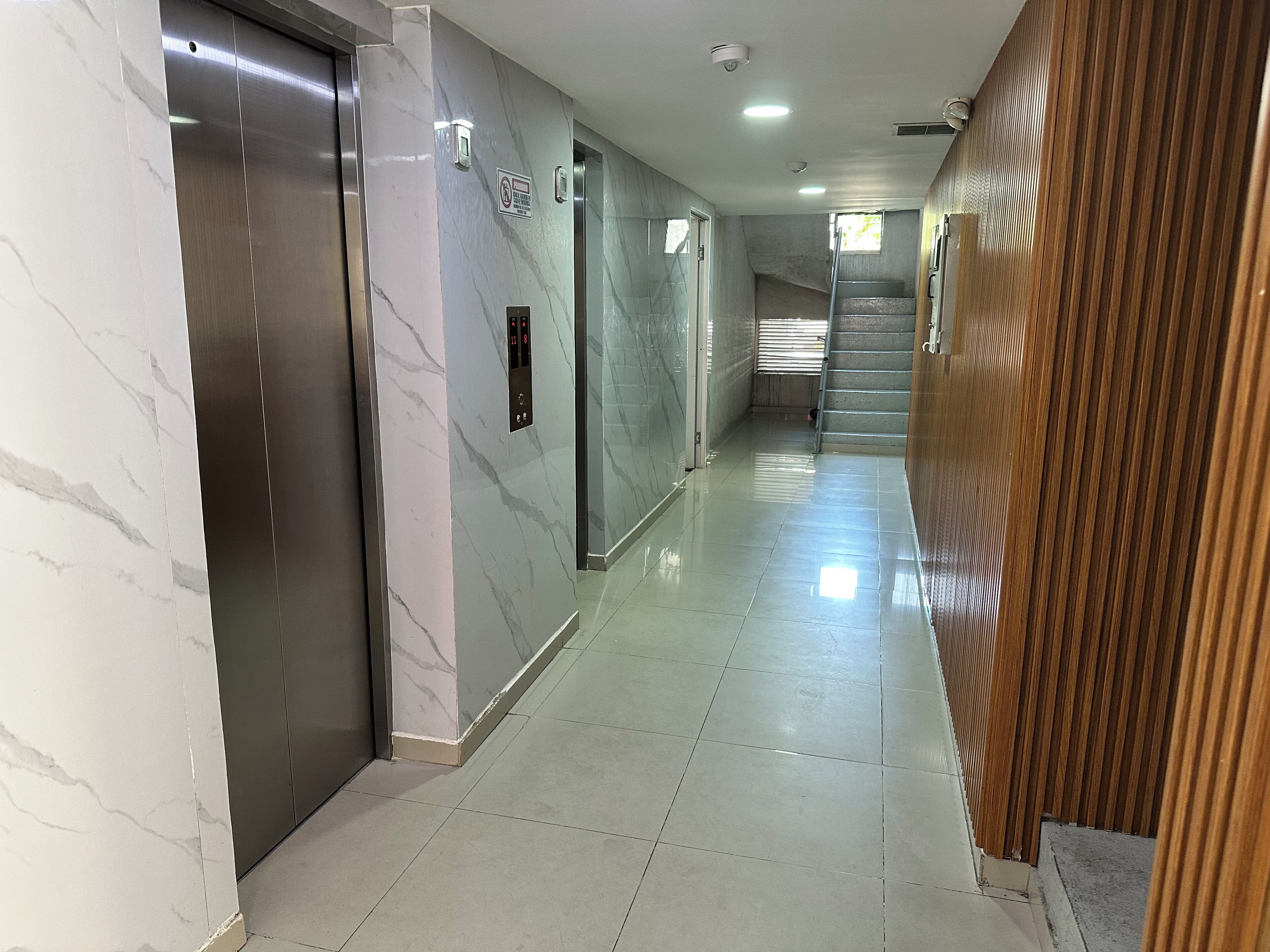 A hallway with marble walls, a wooden panel wall, and a tiled floor.