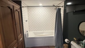 A bathroom with a bathtub, toilet, wooden cabinets, and a tiled wall.
