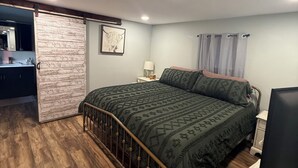 A bedroom with a bed, a nightstand, a lamp, a TV, and a sliding door leading to a bathroom.