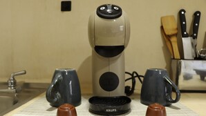 Uma cafeteira numa bancada de cozinha, com duas canecas e duas chávenas.