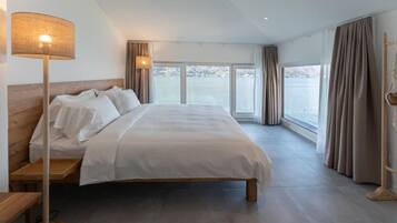 Une chambre d’hôtel avec un grand lit, une lampe de chevet et une vue sur une étendue d’eau par les fenêtres.