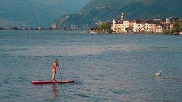 A person paddleboarding on a calm lake with a town and mountains in the background.