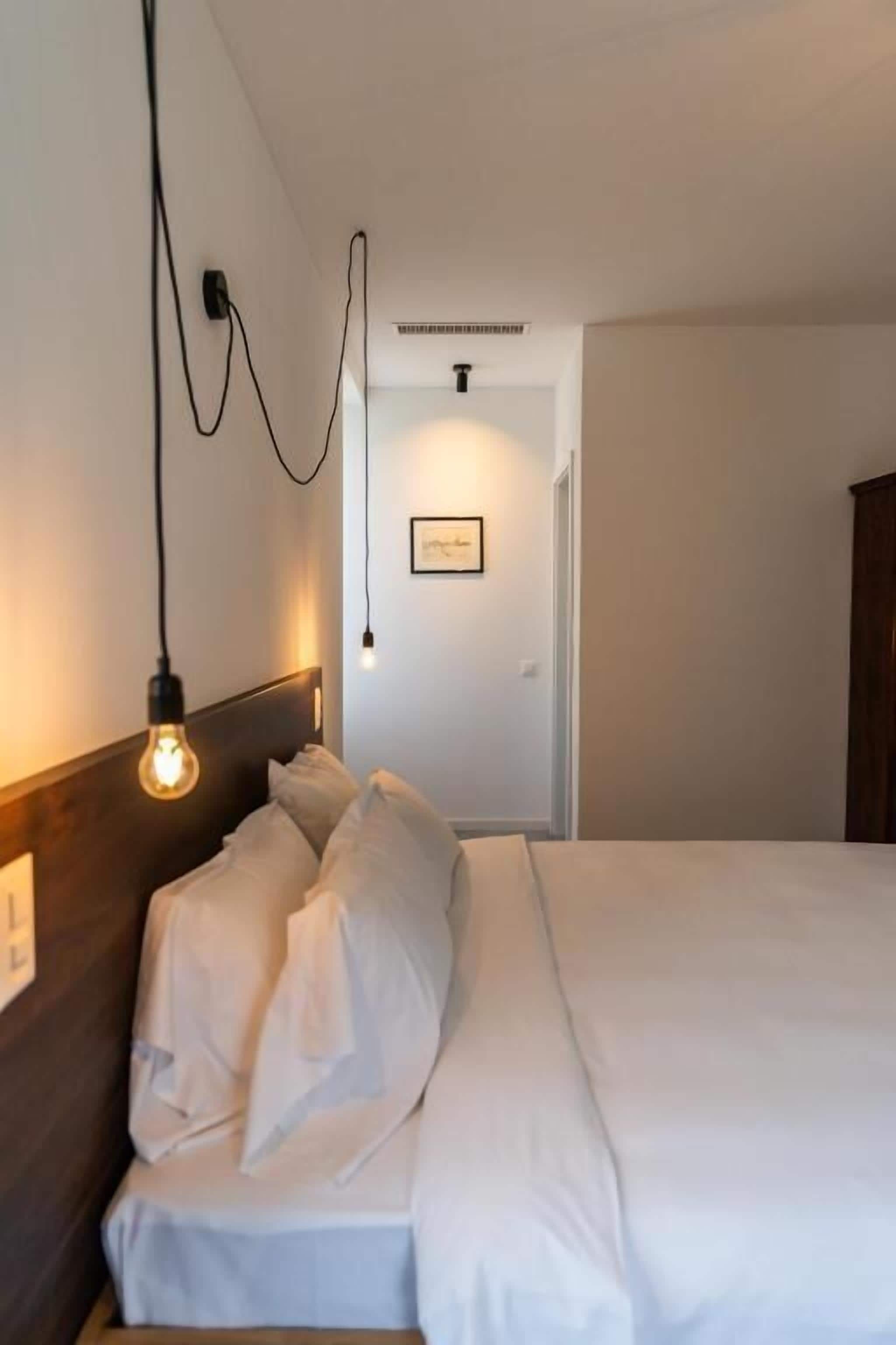 Ein ordentlich bezogenes Bett mit weißen Leinen, eine Wandleuchte und eine Tür im Hintergrund.