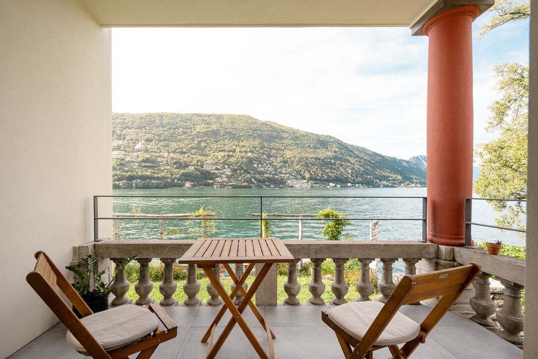 Un balcon avec une table et deux chaises, donnant sur un lac et des collines.