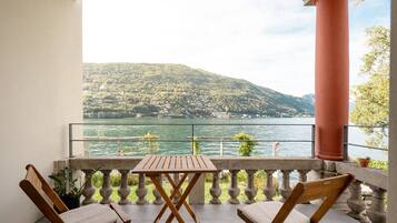 Un balcon avec une table et deux chaises, donnant sur un lac et des collines.