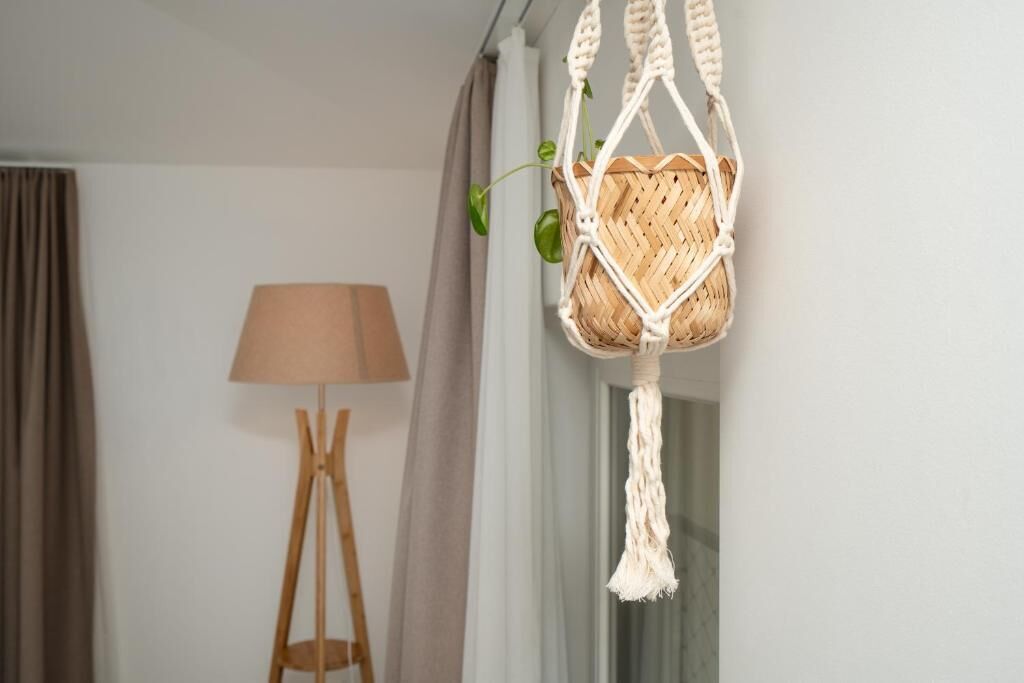 Una cesta colgante de macramé con una planta, una lámpara de pie y una ventana con cortinas.