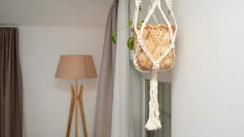 Una cesta colgante de macramé con una planta, una lámpara de pie y una ventana con cortinas.