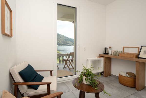 A modern living space with a view of a body of water, a wooden chair, a small table with a plant, and a shelf with decorative items. - Villa Patria B&B (Brusino Arsizio)