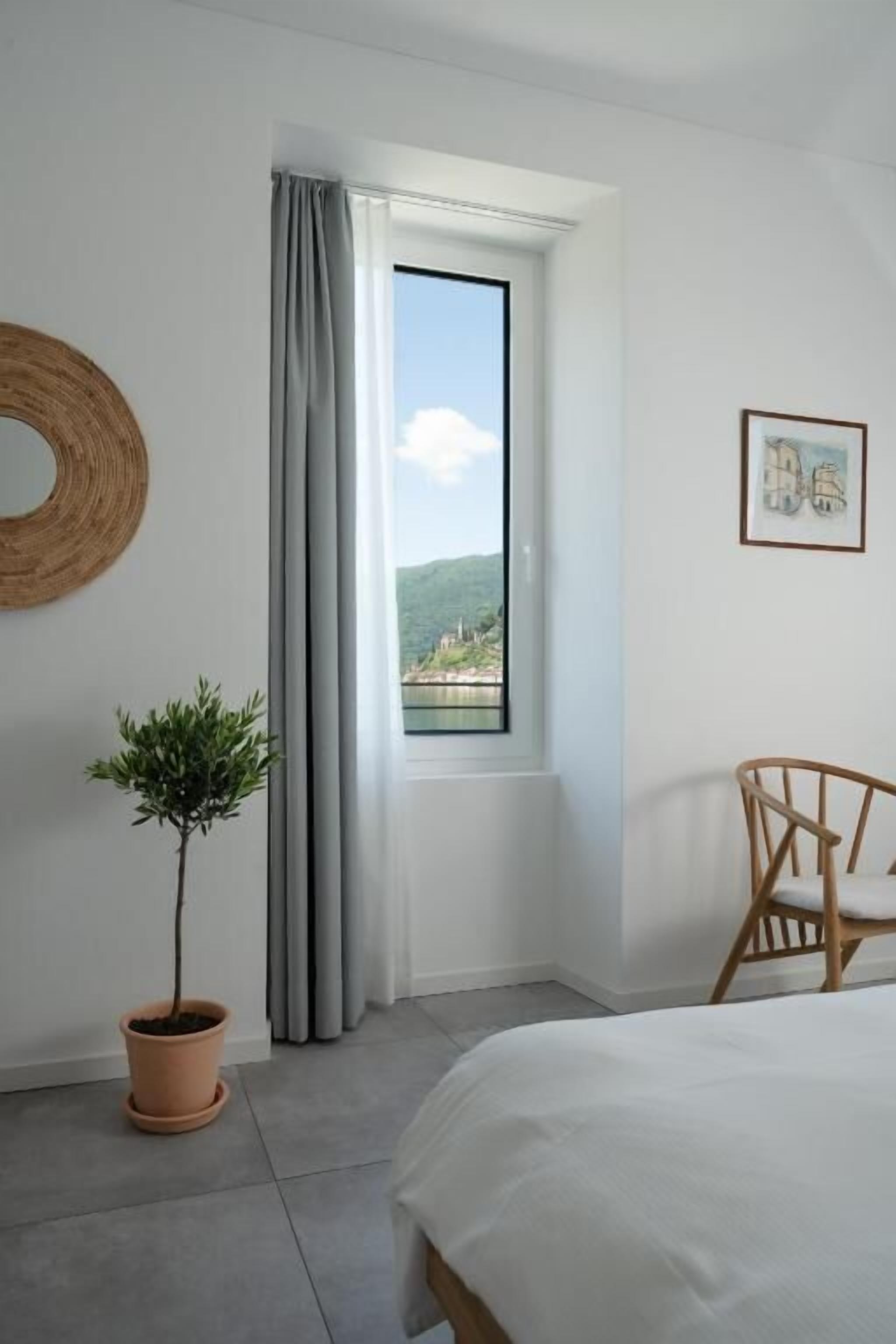 Ein Schlafzimmer mit einem Bett, einem Fenster mit Vorhängen, einer Topfpflanze, einem hölzernen Stuhl und einer runden Wanddekoration.
