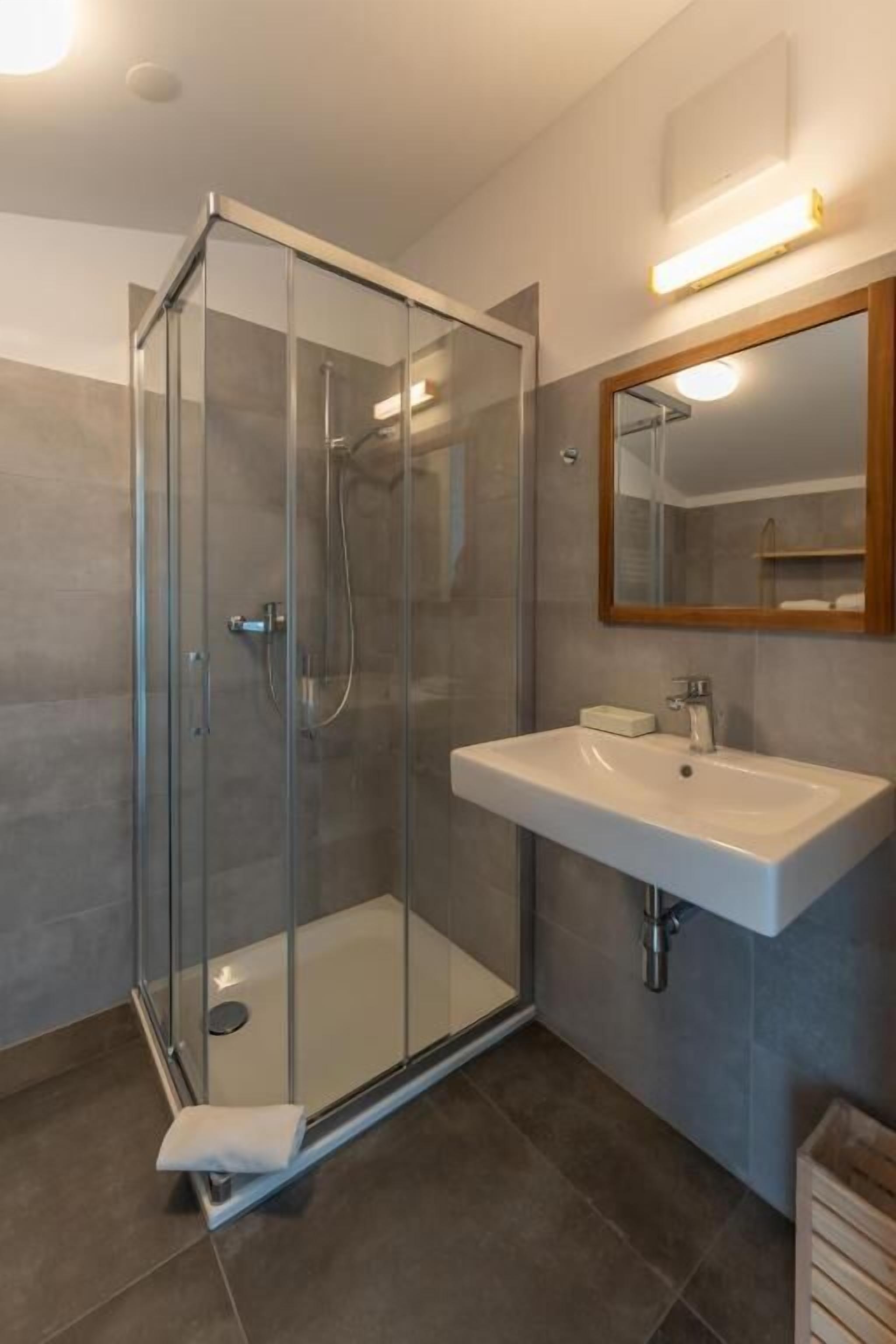 Ein modernes Badezimmer mit einer gläsernen Duschkabine, einem weißen Waschbecken und einem Spiegel mit Holzrahmen.