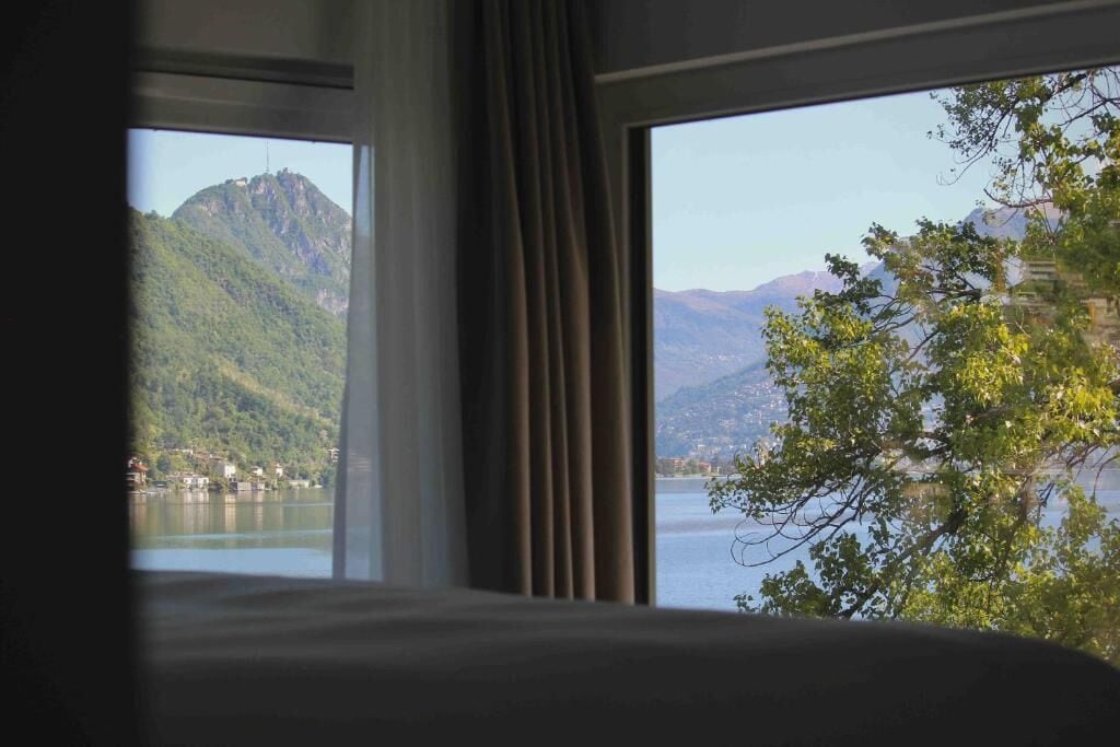 A room with a large window offering a view of a lake and mountains.