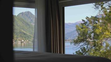 A room with a large window offering a view of a lake and mountains.