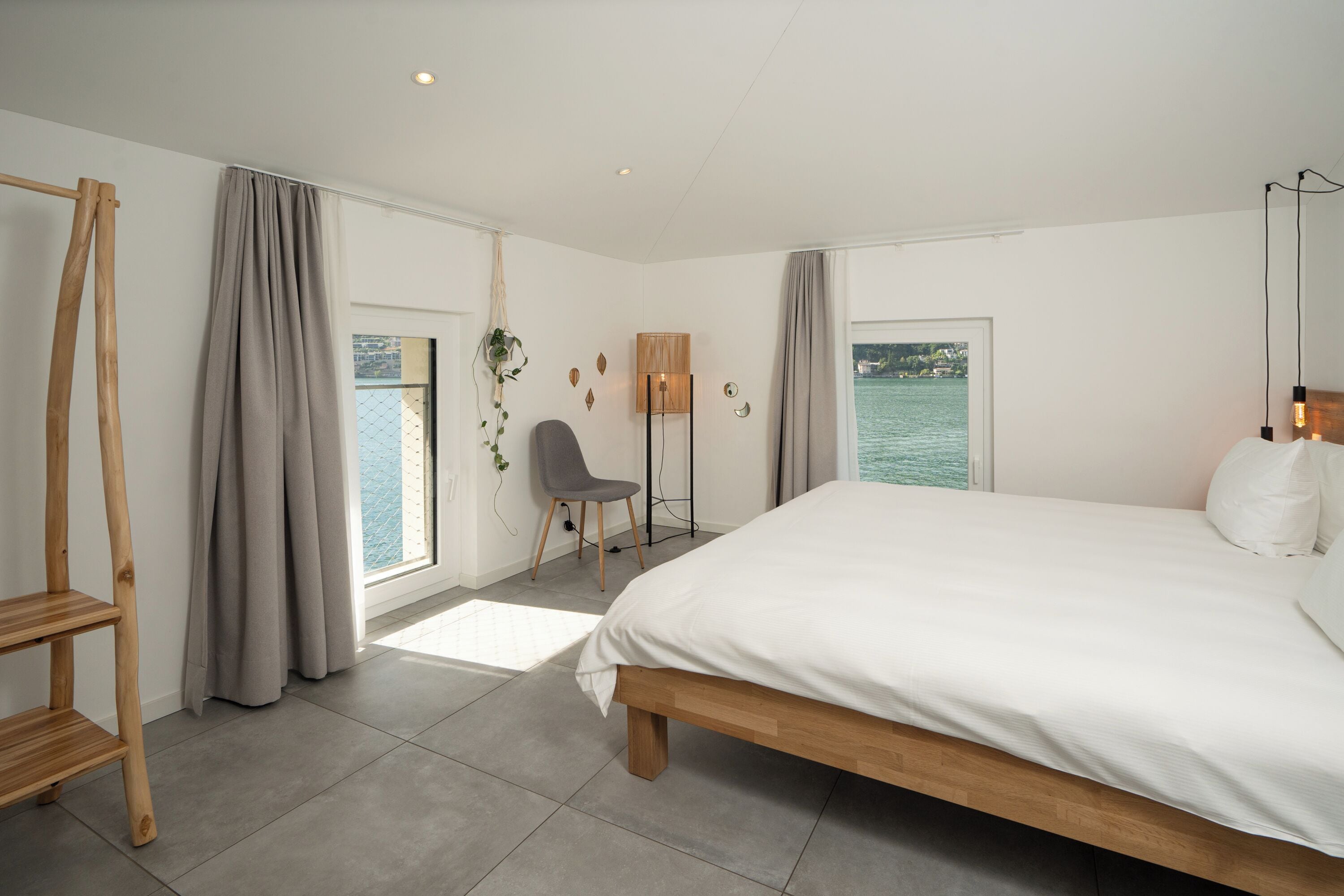 Ein Schlafzimmer mit einem großen Bett, einem Sessel, einem Schreibtisch und Blick auf das Wasser.