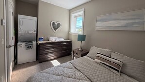 A bedroom with a bed, dresser, vanity, and a washing machine. - Cozy Ocean Gateway at Spirit Bay Pet-friendly (Sooke)