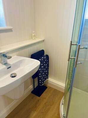 A bathroom with a white sink, a glass shower enclosure, and a blue towel on a chair. - Newly renovated house in Polperro with parking and sea views. (Polperro)