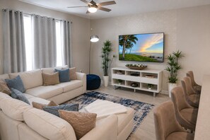 A living room with a sofa, coffee table, and chairs, a TV on the wall, and a ceiling fan. - Luxury Disney Retreat: Private Pool + ChampionsGate Resort Access (Davenport)
