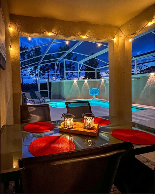 An outdoor dining area with a pool view, a glass table, and red placemats. - Luxury Disney Retreat: Private Pool + ChampionsGate Resort Access (Davenport)