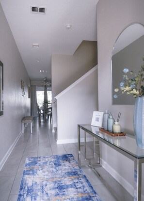 A modern hallway with a glass console table, a blue rug, and a staircase. - Luxury Disney Retreat: Private Pool + ChampionsGate Resort Access (Davenport)