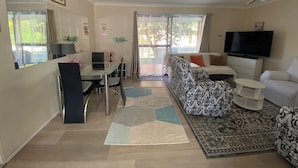 Ein Wohnbereich mit Sofa, Fernseher, Esstisch mit Stühlen und Deckenventilator.