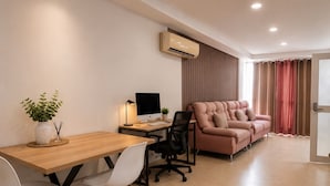 A modern room with a wooden desk, a computer, a comfortable sofa, and a potted plant.