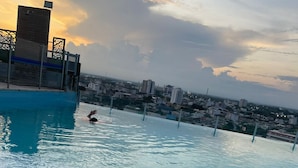 A rooftop pool with a city view, a person swimming, and a person relaxing with feet in the water.