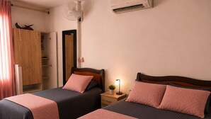 A bedroom with two beds, a wardrobe, a bedside table with a lamp, and an air conditioning unit.