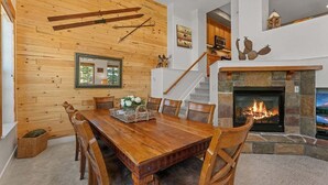 A dining area with a wooden table and chairs, a fireplace, and a staircase leading to an upper level. - Downtown WP Villa 709 I Private Hot Tub I Views I Bunk Room I Desk I Discounted Attractions (Winter Park)