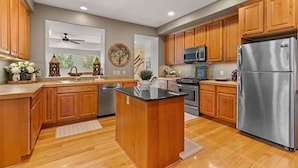 A kitchen with wooden cabinets, a stainless steel refrigerator, a microwave, and a central island. - Downtown WP Villa 709 I Private Hot Tub I Views I Bunk Room I Desk I Discounted Attractions (Winter Park)