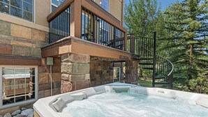 A spa area with a hot tub, stone walls, and a balcony overlooking a forest. - Downtown WP Villa 709 I Private Hot Tub I Views I Bunk Room I Desk I Discounted Attractions (Winter Park)