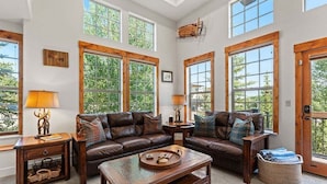 A spacious living room with a large window, a leather sofa, a wooden coffee table, and a wicker basket. - Downtown WP Villa 709 I Private Hot Tub I Views I Bunk Room I Desk I Discounted Attractions (Winter Park)
