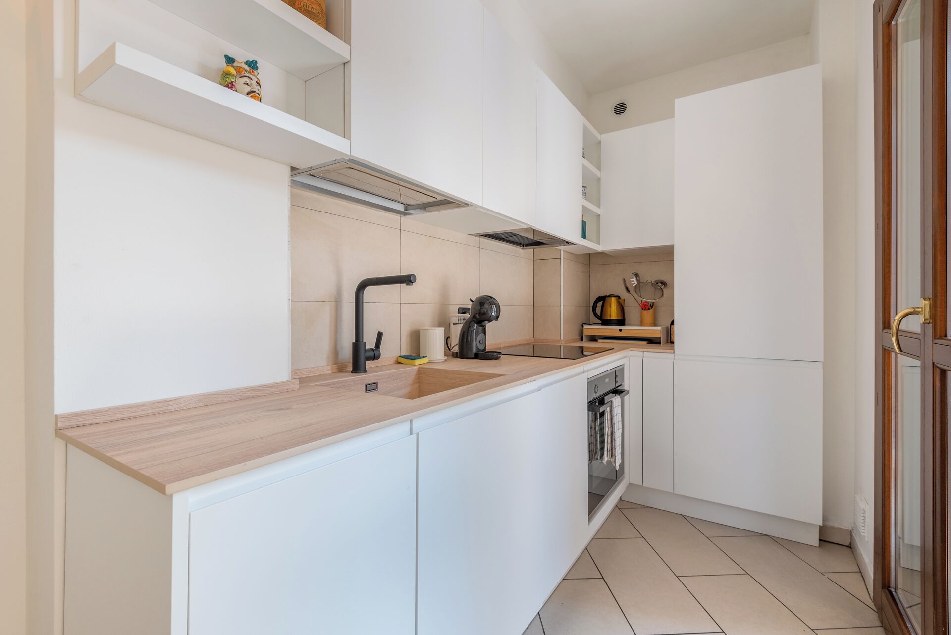 Una cucina moderna con mobili bianchi, un piano di lavoro in legno, un rubinetto nero, un bollitore e una macchina da caffè.