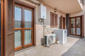 A residential building with a central air conditioning unit, a water heater, and a window with wooden shutters.